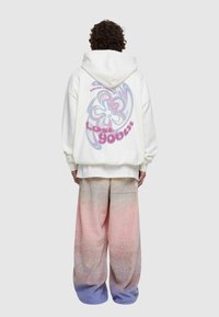 Vit oversized hoodie med en färgglad abstrakt design på ryggen, kombinerad med gradientpastell byxor med vida ben som övergår från rosa till blå.