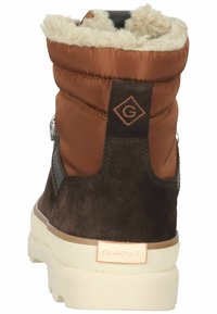 Brown suede and nylon ankle boots with cream faux fur lining and a white rubber sole. Features stitched accents and a logo on the back.