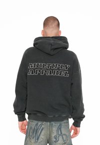 Černá mikina s kapucí se textem "MULTIPLY APPAREL" na zádech. Má volný střih a měkkou, jemně texturovanou tkaninu.