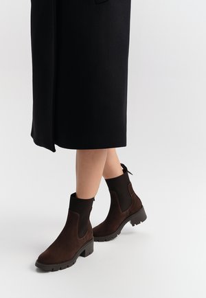 Ankle boots in dark brown suede with ribbed elastic sides, sturdy rubber sole, and a pull tab at the heel for easy wear.