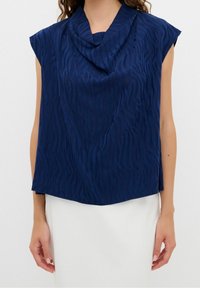 Top blu navy a maniche corte realizzato in tessuto testurizzato con un colletto drappeggiato e un sottile motivo a zigzag, caratterizzato da una vestibilità comoda.