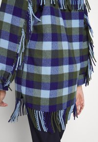 Ternet stofjakke i nuancer af blå, grøn og lilla med frynsekant og afslappet pasform. Tekstureret uldblandet materiale.