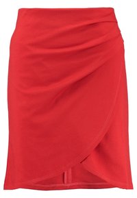 Jupe enveloppante rouge en tissu doux, avec un devant drapé, un ourlet asymétrique et des détails de couture visibles. Texture lisse.