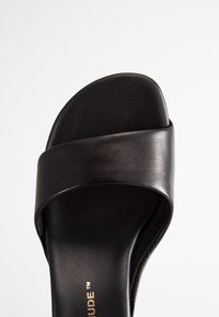 Ciabatta nera in pelle liscia con una fascia ampia e un plantare contornato. Presenta un design minimalista con un dettaglio in logo metallico.