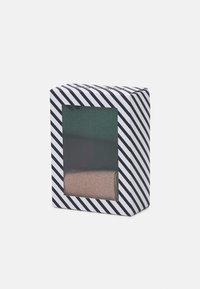 Pakningen indeholder to genstande: et grønt, glitrende stof og et beige stof. Æsken har en klar front og diagonale striber i sort og hvid.