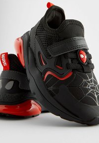 Baskets de sport noires avec des accents rouges, tige en maille, motif en toile d'araignée et détail du logo Spider-Man. Sangle à velcro pour un maintien sécurisé.