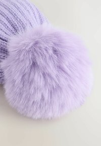 Lila gestrickter Stoff mit einem großen, flauschigen Pompon aus weichem Kunstfell, vor einem hellen, neutralen Hintergrund.