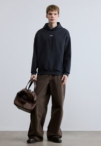 Σκούρο μπλε φούτερ με κουκούλα, εμπρός τσέπη και κορδόνια, σε συνδυασμό με ελεύθερο παντελόνι καφέ και καφέ δερμάτινη τσάντα. Μινιμαλιστικός σχεδιασμός και καθαρές γραμμές.