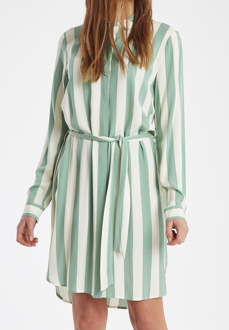 Abito a righe verde e bianco, realizzato in tessuto leggero. Presenta un colletto, maniche lunghe e una cintura annodata in vita.