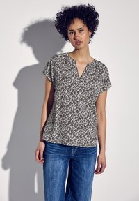 Top a maniche corte in nero e bianco sporco con un motivo floreale, caratterizzato da un scollo a V e una vestibilità informale, abbinato a jeans blu.