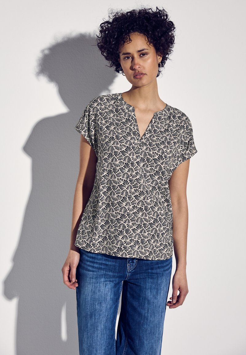 Top a maniche corte in nero e bianco sporco con un motivo floreale, caratterizzato da un scollo a V e una vestibilità informale, abbinato a jeans blu.