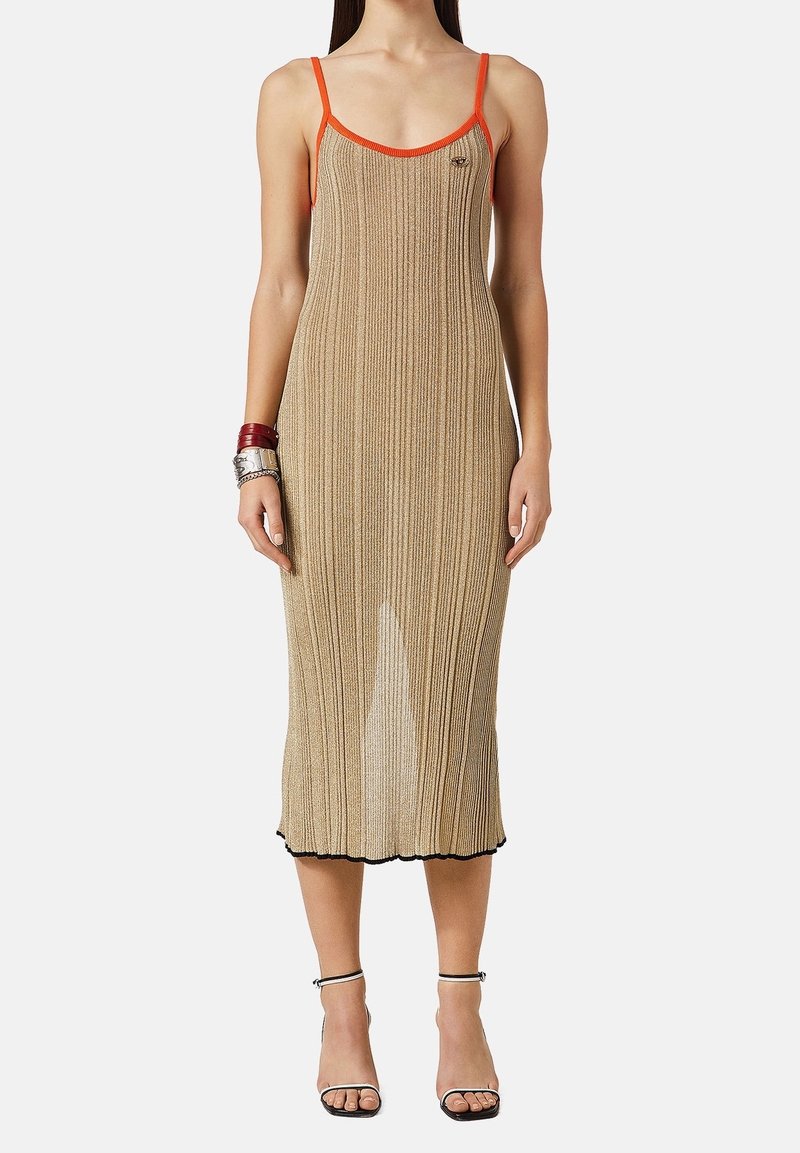 Femme portant une robe midi en maille côtelée beige avec une bordure orange, des sandales noires et des bracelets superposés au poignet gauche, devant un fond uni.
