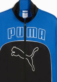 Zila un melna treniņu jakas ar augstu apkakli, priekšējo rāvējslēdzēju un izteiksmīgu balto Puma logotipu uz krūtīm. Izgatavota no slidena auduma.