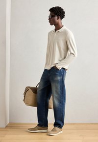 Beige langermet polo skjorte, mørkeblå jeans med falmede detaljer, lysebrune semskede sko, og en lysbrun skulderveske plassert ved siden av.