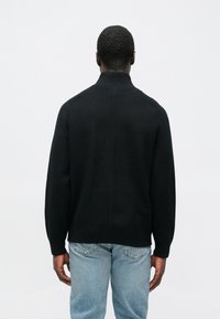 Μαύρο πλεκτό πουλόβερ με ψηλό γιακά, με άνετη εφαρμογή και ριμπ μανσέτες. Φορεμένο με ανοιχτόχρωμο μπλε τζιν για αντίθεση.