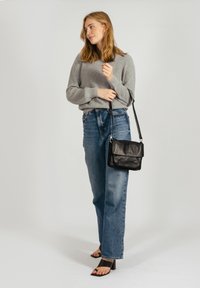 Un pull en tricot gris, un jean bleu taille haute, un sac à bandoulière noir et des sandales à talons carrés noires. Design simple avec une coupe décontractée.