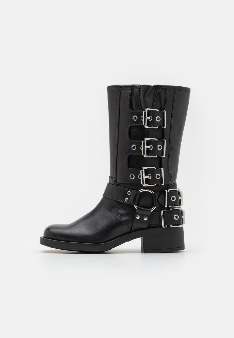 Black leather boot with a tall shaft, featuring multiple silver buckles and straps, a circular accent, and a chunky heel. Matte finish.