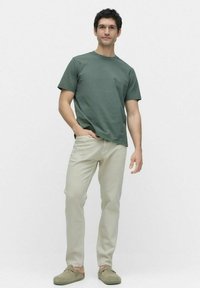 Grön bomull t-shirt, avslappnad passform, matchad med ljusbeiga byxor. Mjuk textur. Bruna slip-on skor. Enkelt design, inga synliga mönster.