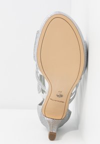 Sandale à talons hauts pailletée argentée vue de la semelle avec semelle extérieure beige, nom de la marque et taille 37.