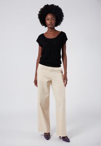 Top negro de punto con mangas cortas, combinado con pantalones de pierna ancha en color beis. El modelo lleva tacones morados con adornos decorativos. Textura suave en toda la prenda.