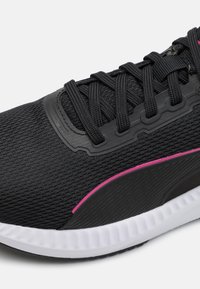 Zapatilla deportiva negra con parte superior de malla, acentos texturizados, detalles en rosa, cordones negros y una suela blanca acolchada.