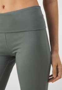 Høyt liv, tettsittende leggings i et dempet grønt stoff. Glatt tekstur; sømløst design med bred midjebånd for komfort.