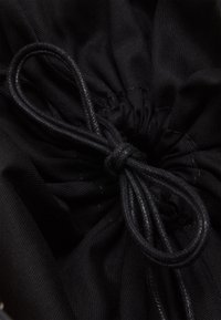 Svart dragsäcksinredning med tätt vävt tyg, snörs ihop med en flätad svart snodd som skapar en samlad textur.