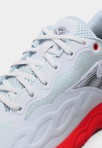 Λευκό και γαλάζιο αθλητικό παπούτσι με λευκά κορδόνια, ύφασμα από δίχτυ, λογότυπο στη γλώσσα και φωτεινή κόκκινη σόλα με υφή σχεδίου.