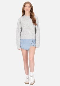 Szürke kötött pulóver színes foltokkal, kerek nyakkivágással és bordás aljjal, farmerfátyollal és fehér tornacipővel párosítva.