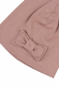 Rosa stickad mössa med en texturerad yta, prydd med en stor rosett på ena sidan. Designen är enkel och rundad.