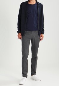 Námornícky pletený cardigan přes námornícké tričko, doplněný šedými slim-fit kalhotami a bílými teniskami. Jednoduchý design s minimem kovových doplňků.
