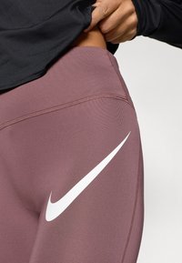 Κολάν Nike σε χρώμα μωβ με λευκό λογότυπο Swoosh. Διαθέτει λεία, ελαστική ύφανση και διακοσ μητική ραφή κατά μήκος των ραφών.