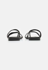Sandale negre cu o talpă netedă, având curele împletite intricate și un design minimalist. Curelele sunt plate și flexibile.