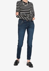 Paita pitkillä hihoilla, jossa on mustavalkoraidat, yhdistetty tummansinisiin farkkuihin, joissa on slim fit -leikkaus ja pienen pieni kuluminen helmassa. Mustat loafer-kengät viimeistelevät asun.