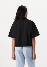 Top corto nero con colletto, con pizzo sulle maniche e sull'orlo. Abbinato a pantaloni a righe blu chiaro.