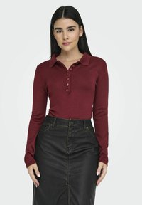 Bordeaux long-sleeve polo shirt met een geknoopte placket en zachte stof, gecombineerd met een zwarte leren rok met gele stiksels.