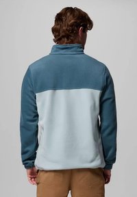 Giacca in pile con un design color-block, con una sezione superiore di colore blu scuro e una sezione inferiore di colore blu chiaro. Collo alto e polsini elasticizzati.