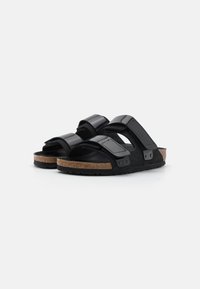 Sandali neri con due eleganti cinturini regolabili e una soletta in sughero, dotati di suola in gomma texture e forma arrotondata per il massimo comfort.