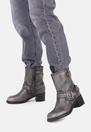 Bottes d'ankle en cuir gris, finition mate, bout rond, boucles et sangles en métal argenté, petit talon empilé, zips détaillés sur les côtés.