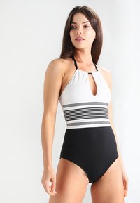 Maillot de bain noir et blanc style halter avec un devant en trou de serrure, présentant des rayures horizontales sur la poitrine et un bas noir uni. Texture lisse.