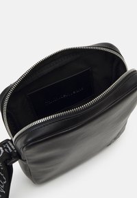 Borsa nera in pelle con chiusura a zip. Fodera interna in tessuto nero. Presenta una tracolla stampata e un'etichetta del marchio in pelle all'interno.