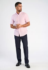 Camicia rosa chiaro a maniche corte con bottoni, pantaloni blu scuro e scarpe nere. La camicia ha una vestibilità morbida e un tessuto a trama.