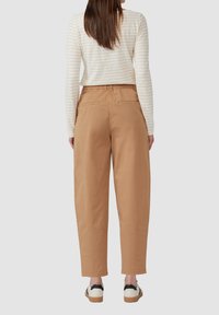 Maglietta a maniche lunghe a righe beige chiaro abbinata a pantaloni larghi a vita alta di colore marrone chiaro con tasche posteriori e una texture liscia.