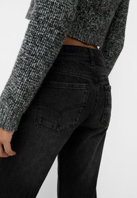 Jeans de mezclilla negra con una cintura ajustada y piernas anchas, combinados con un suéter de punto gris texturizado que cuenta con mangas largas y un corte corto.
