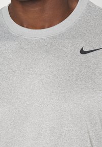 Grå bomullströja med en klassisk rund halsringning, med en diskret svart Nike-logga på den övre vänstra sidan. Slät textur.