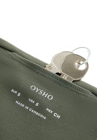 Deux clés en argent sur un anneau placées dans la poche d’un vêtement Oysho vert olive, taille petite, fabriqué au Cambodge.