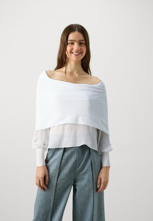 Witte blouse met kapmouw ontwerp en doorzichtige textuur, gelaagd over een lichtgewicht, semi-doorzichtige blouse. Combi ne met lichtblauwe, wijde pantalon.