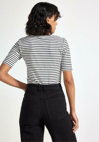 Sort-hvid stribet t-shirt lavet af bomuld, semi-tilpasset med korte ærmer. Parret med højtaljede sorte jeans med to baglommer.