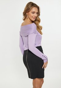 Top lila cu mâneci lungi, cu design off-shoulder și detaliu drapat; combinat cu o fustă neagră ce prezintă un acccent de fermoar aurie pe lateral.