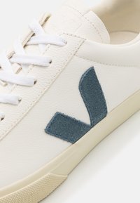 Λευκά δερμάτινα αθλητικά παπούτσια με υφή, φέρουν λογότυπο από σκούρο μπλε suede. Διαθέτουν λευκές κορδόνες και μπεζ καουτσούκ σόλα με υφή.